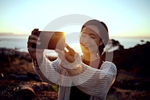 Hiking, selfie and Asian woman on mountain with sunset sky, smile and relax in nature on holiday adventure. Digital