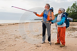 Hiking tourism adventure. Senior couple man woman enjoying outdoor recreation hiking on beach. Happy old people