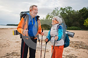 Hiking tourism adventure. Senior couple man woman enjoying outdoor recreation hiking on beach. Happy old people