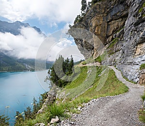 Hiking trail above the Oeschinensee, under overhanging rocks of a steep rock face. Danger of rock falls and avalanches, swiss alps