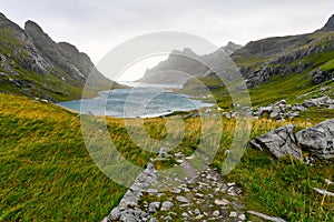 Hiking trail leading to a beautiful bay surrounded by mountains and a small village near Bunes Beach and Vinstad on Lofoten Island