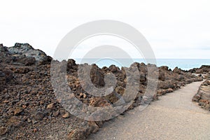 Hiking trail in Los Hervideros. Southwest coast, rugged volcanic landscape, caves and red lava hills. Lanzarote