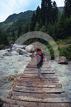 Hiking trail to Shdugra Waterfall, through green dense forest with a female traveler. Woman tourist standing on wooden bridge over