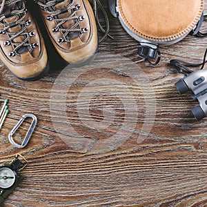 Hiking or travel equipment with boots, compass, binoculars, flask on wooden background. Active lifestyle concept.