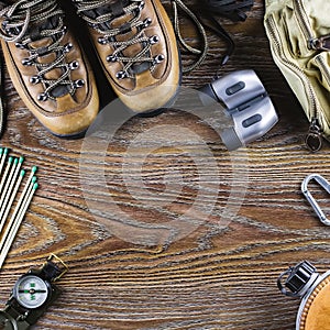 Hiking or travel equipment with boots, compass, binoculars, matches on wooden background. Active lifestyle concept.
