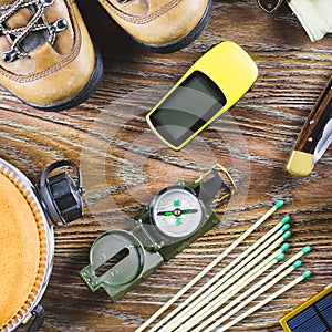 Hiking or travel equipment with boots, compass, binoculars, matches on wooden background. Active lifestyle concept.