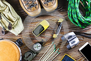 Hiking or travel equipment with boots, compass, binoculars, matches on wooden background. Active lifestyle concept.