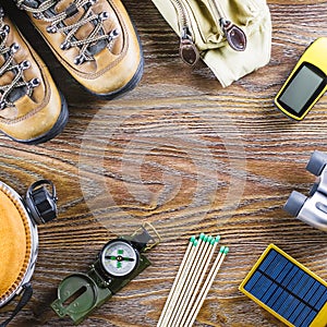 Hiking or travel equipment with boots, compass, binoculars, matches on wooden background. Active lifestyle concept