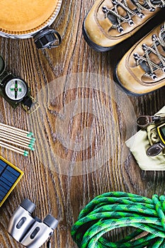 Hiking or travel equipment with boots, compass, binoculars, matches on wooden background. Active lifestyle concept