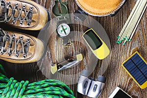 Hiking or travel equipment with boots, compass, binoculars, matches on wooden background. Active lifestyle concept