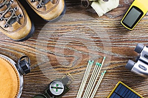 Hiking or travel equipment with boots, compass, binoculars, matches on wooden background. Active lifestyle concept