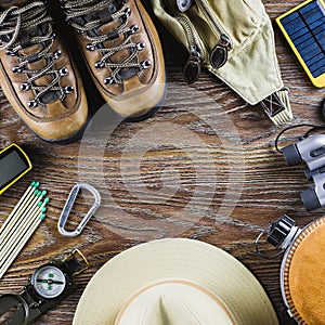 Hiking or travel equipment with boots, compass, binoculars, matches on wooden background. Active lifestyle concept.