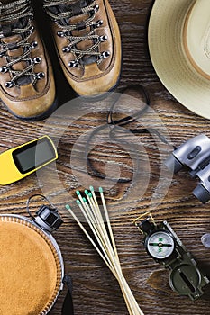 Hiking or travel equipment with boots, compass, binoculars, matches on wooden background. Active lifestyle concept.