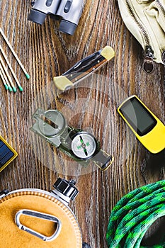 Hiking or travel equipment with boots, compass, binoculars, matches on wooden background. Active lifestyle concept