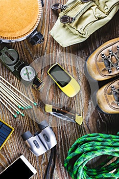 Hiking or travel equipment with boots, compass, binoculars, matches on wooden background. Active lifestyle concept