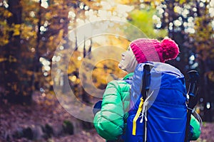 Hiking woman with backpack looking at inspirational autumn golden woods