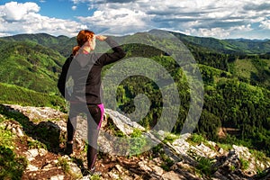 Turistika žena pri pohľade z vrcholu kopca na zelený les a hory