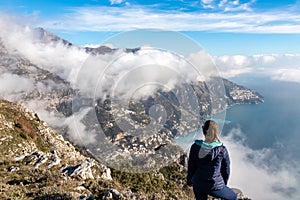 Hiking woman with scenic view from Monte Comune on clouds covering the coastal town Positano at the Amalfi Coast, Campania, Italy.