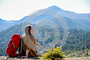 Hiking woman sit on seaside rock. Lady hiker with backpack on top of the mountain and enjoying valley view. Active