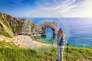 A hiking woman stands in front of the famous Durdle Door beach