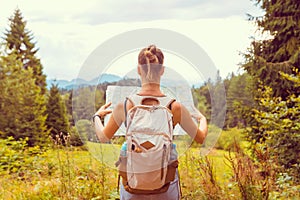 Hiking woman traveler with backpack checks map to find directions in wilderness area, real explorer. Travel Concept