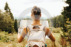 Hiking young woman traveler with backpack checks map to find directions in wilderness area, real explorer