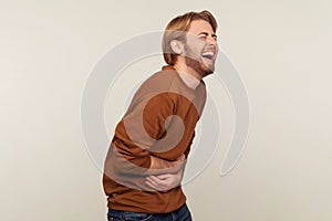 Hilarious laughter. Portrait of amused man with beard wearing sweatshirt holding belly and laughing out loud