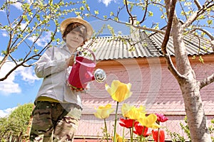 Ð¡hild in the garden watered flowers from a watering can in the summer. Kid gardener has fun working in the park in spring. A boy