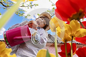 Ð¡hild in the garden watered flowers from a watering can in the summer. Kid gardener has fun working in the park in spring. A boy