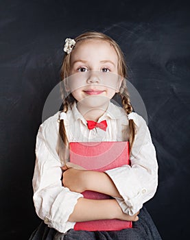 Ð¡hild girl in school uniform clothes with book on chalk board