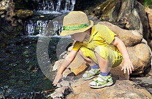 Ð¡hild kid boy 3 year in straw hat and a yellow T-shirt, touches his hand to the water in the pond. Vacations and Walking in zoo