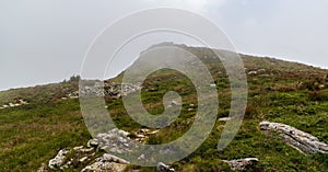 Hill covered by meadow with stones and rock formation on summit during cloudy day - Varful Mutu hill in Valcan mountains in photo