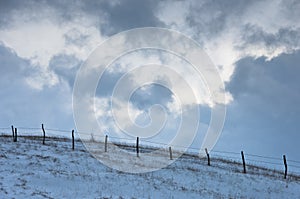 Hill with a fence covered with snow under dramatic clouds at winter, mountain Kozomor