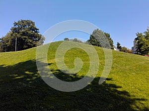 Hill with grass and shadows of trees with clear blue sky at summer day, beautiful Green grass field calm summer day, landscape in