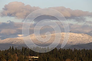 Hill located at a higher altitude covered in fresh snow whereas there is no snow in the city below