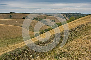 Hills covered with yellow grass under rainy clouds