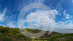 Hills with green grass and trees on the coast with blue sky and clouds.