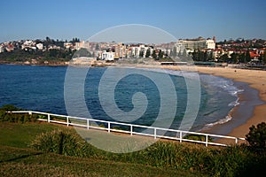 Hillside town and beach on waterfront. Scenic landscape with grass, shrubs and white fences on hilltop by sea in Sydney, Australia