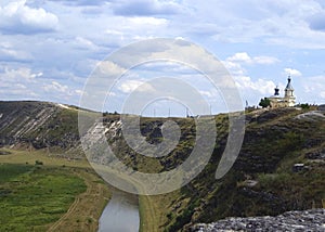 Hilltop church, rocky riverbank, green fields, sky in the clouds