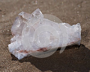 Himalayan clear quartz cluster with hematite inclusions on wet sand on the beach