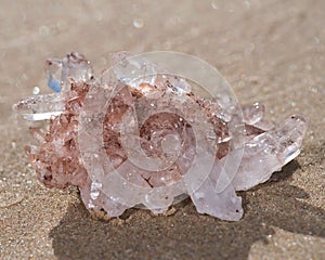 Himalayan clear quartz cluster with hematite inclusions on wet sand on the beach