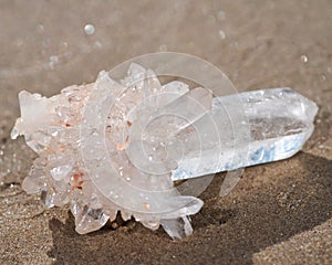 Himalayan clear quartz cluster with hematite inclusions on wet sand on the beach