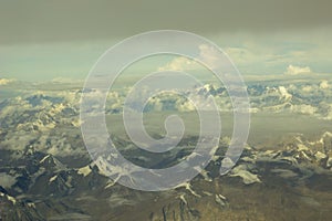 Himalayan desert mountain valley with snowy peaks under a blue sky with white and gray clouds. Aerial view