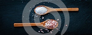 Himalayan pink salt and sea salt in wooden spoons on dark background, top view