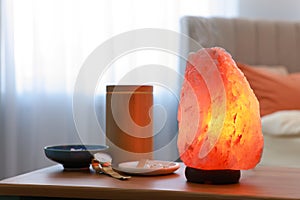 Himalayan salt lamp, air ionizer and accessories on wooden table in bedroom photo