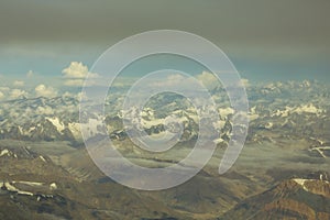 Himalayan yellow desert mountain valley with snowy peaks under a blue sky with white and gray clouds aerial view