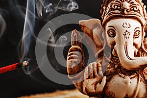 Hindu god Ganesh on a black background. Rudraksha statue and rosary on a wooden table with a red incense stick and incense smoke