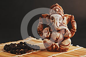 Hindu god Ganesh on a black background. Statue with incense smoke aromo sticks