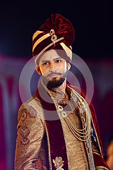 Hindu groom wedding day on stage wearing maroon dress and turban