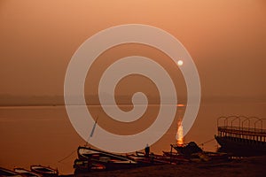 A hindu man praying during sunrise on the river Ganges in Varanasi, India. Fog, seagulls and boat silhouettes